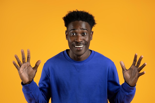 Amazed young african american guy raising hands up on yellow