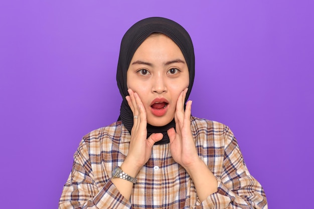 Amazed young asian woman in plaid shirt looking at camera with
wow face expression isolated on purple background