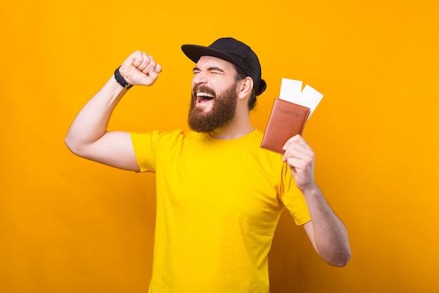 Amazed young bearded hipster man celebrating holiday and holding passport with tickets