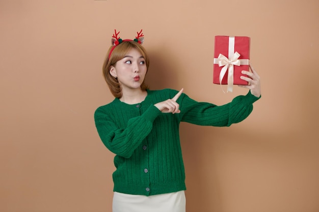 Amazed young girl in fun decorative deer horns on head with red gifts presents