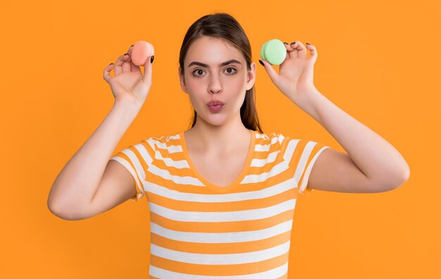 Amazed young girl with macaron on yellow background