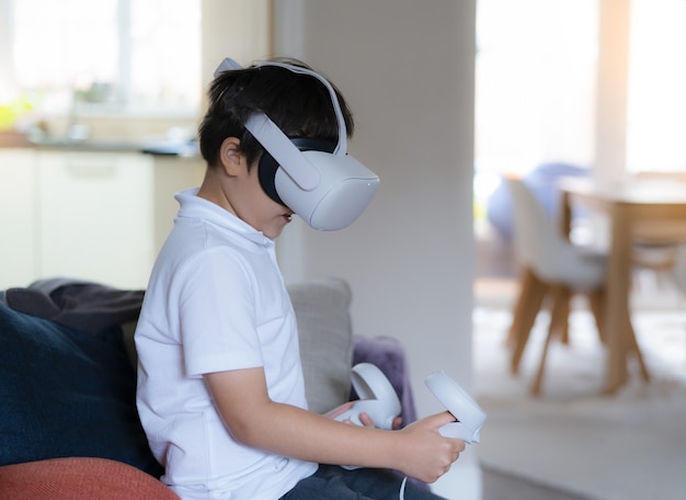 バーチャルリアリティゴーグルを身に着けている驚いた幼い子供。 VRヘッドセットで見てビデオゲームをプレイする感情的な少年。リビングルームで3Dガジェットを体験している混血の少年の肖像画。