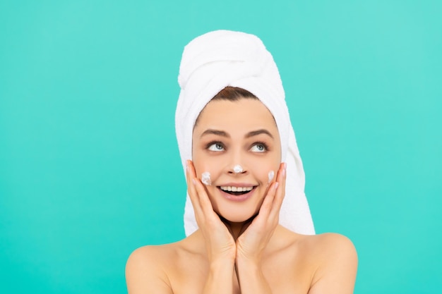 Amazed young lady applying face cream on blue background