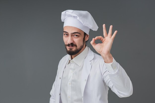 Изумленный молодой мужчина, итальянский красивый шеф-повар. Он жестикулирует вкусной вывеской.