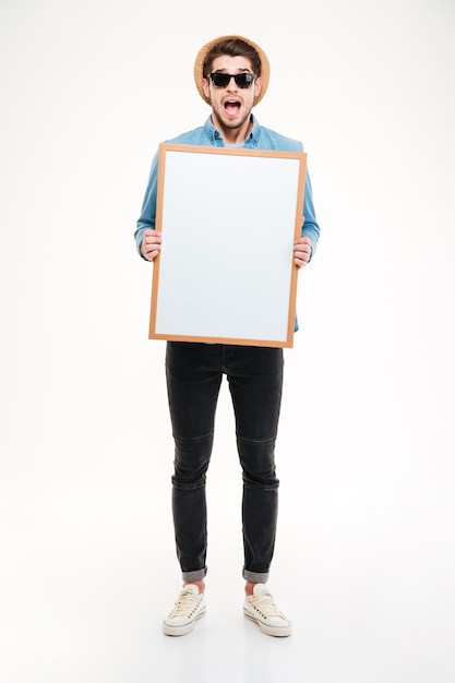 Amazed young man with mouth opened shouting and holding blank whiteboard