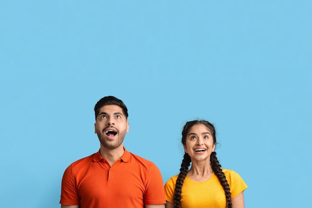 Amazed young middle eastern couple looking up at copy space with excitement