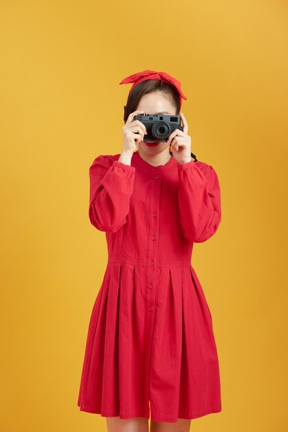 黄色の背景の上にカメラを持って驚いた若いきれいな女性