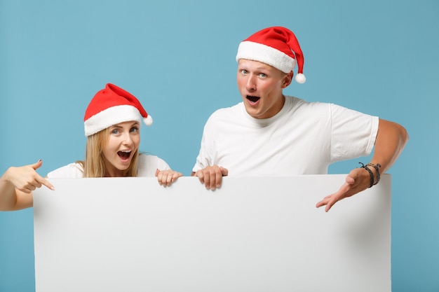 Amazed young Santa couple friends guy and woman in Christmas hat 