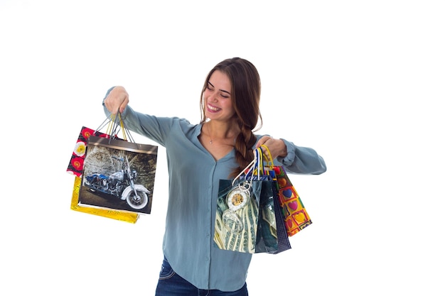 Amazed young woman in blue blouse holding varicolored shopping bags in her hands in studio