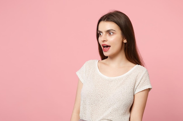 Amazed young woman in casual light clothes posing isolated on pastel pink background, studio portrait. People sincere emotions lifestyle concept. Mock up copy space. Looking aside, keeping mouth open.