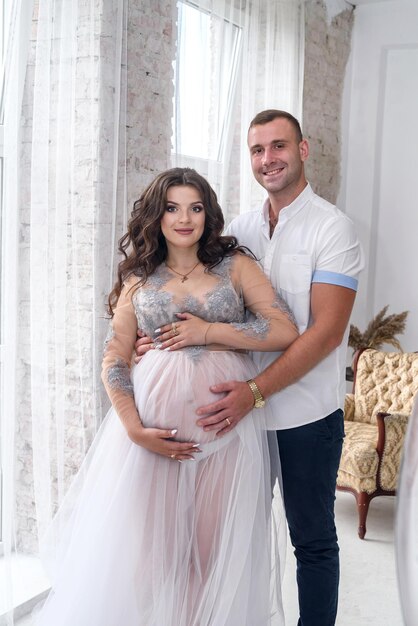 Amazing attractive and pregnant pair posing in studio near window