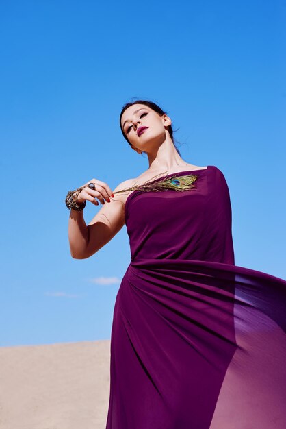 Amazing beautiful brunette woman with the Peacock feather in purple fabric in the desert