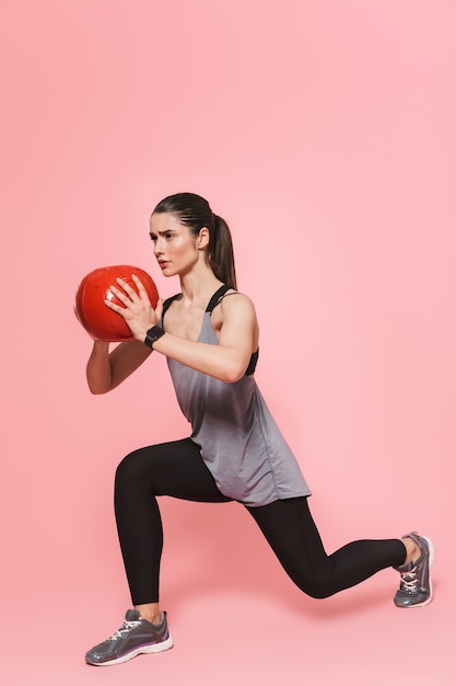 Amazing beautiful young pretty fitness woman make sport exercises with ball isolated over pink wall