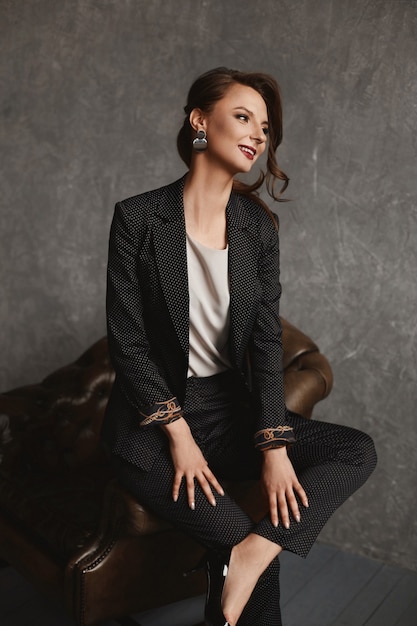 Amazing beauty a gorgeous model girl with perfect makeup and hairdo in stylish suit posing in the vintage armchair