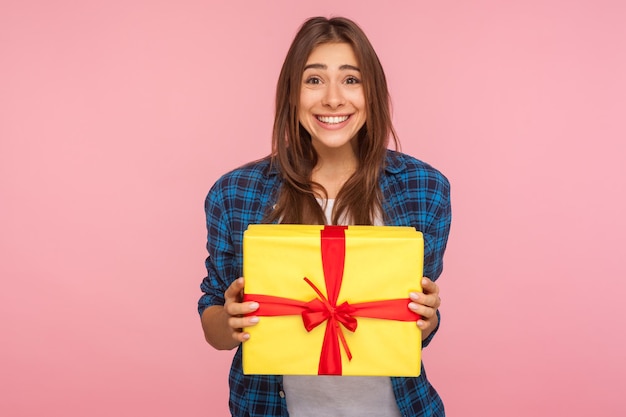 Amazing bonus holiday present Portrait of extremely happy girl in checkered shirt holding wrapped box and looking at camera with toothy smile excited about unexpected gift studio shot isolated