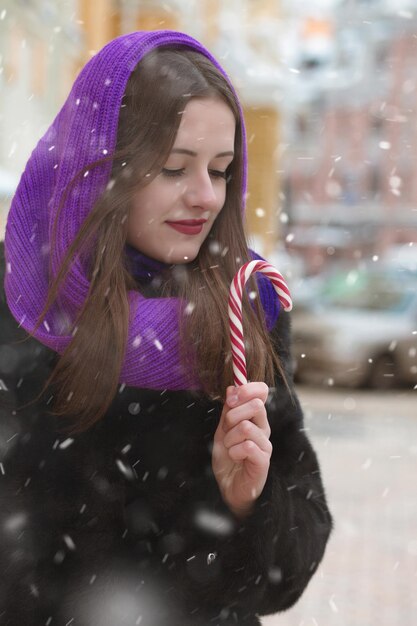 雪片のある通りでカラフルなキャンディーを楽しんでいる素晴らしいブルネットの女性