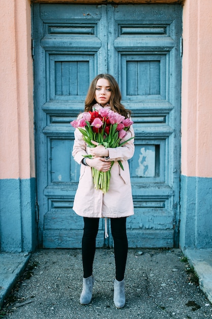 amazing brunette woman standing in front of old  blue door with a bouquet of tulips.