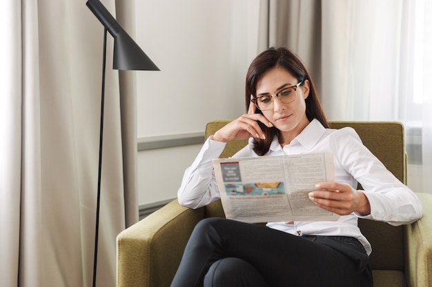 amazing concentrated beautiful young business woman in formal wear clothes indoors at home reading newspaper.