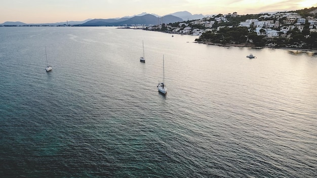 Amazing drone view of modern yachts sailing on rippling surface of sea near coastal town at sunset in Mallorca Spain