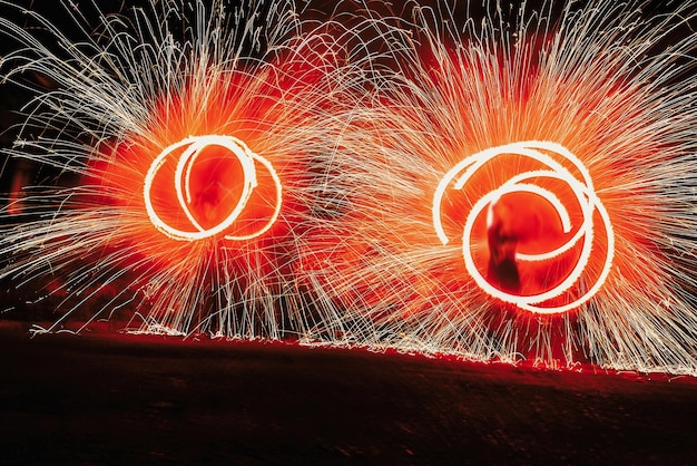 Foto incredibile spettacolo di fuoco di notte al festival o alla festa di matrimonio i danzatori del fuoco oscillano con il fuoco rosso rotante e l'uomo si destreggia con scintille luminose durante lo spettacolo di fuoco notturno e l'intrattenimento