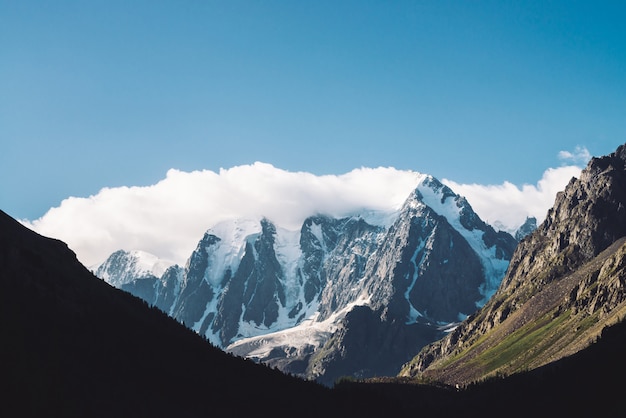 Amazing glacier under blue sky. Mountain range with snow. Huge cloud on giant wonderful snowy mountains. Atmospheric minimalist moody landscape of majestic nature of highlands in matte tones.