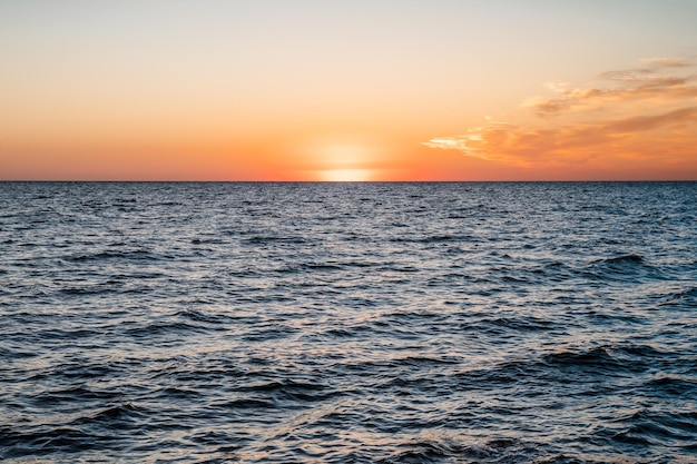 空と水の間にオレンジ色の夕日の太陽の地平線が並ぶ海の素晴らしい風景