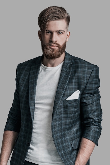 Amazing look! Attractive man with long hair and beard looking at camera while standing against grey background