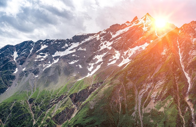 Удивительный горный ландшафт с красочным ярким закатом солнца на облачном небе естественный фон для путешествий на открытом воздухе Горный пейзаж с заснеженными вершинами Идиллический горный фон