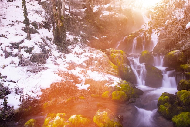 Удивительный природный ландшафт, красивый водопад с солнечным светом в глубоком зимнем лесу