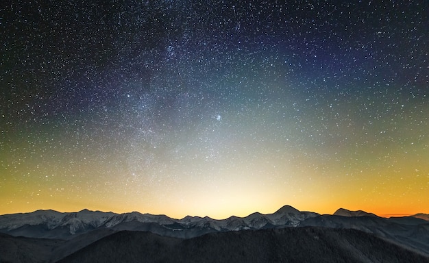 Incredibile paesaggio montano notturno con alte vette e cielo stellato luminoso sopra.