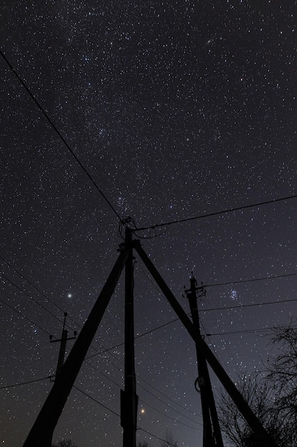 Amazing night sky with stars and power towers with lines in countryside Beautiful starry sky and electricity wires