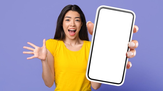 Удивительное предложение Удивленная азиатка показывает пустой экран смартфона
