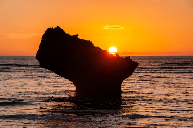 Amazing orange sunset descending on the horizon behind a coastal rock formation.