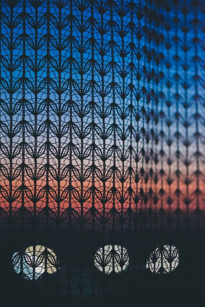 Amazing romantic sunset in window behind silhouettes of tulle texture. Wonderful grapefruit blue dawn sky from window through patterned curtain.