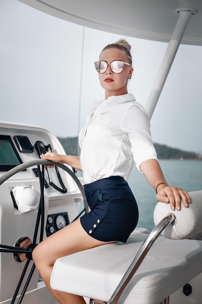 Incredibile donna magra sexy in camicetta e pantaloncini è seduta al volante di uno yacht e guida, ritratto