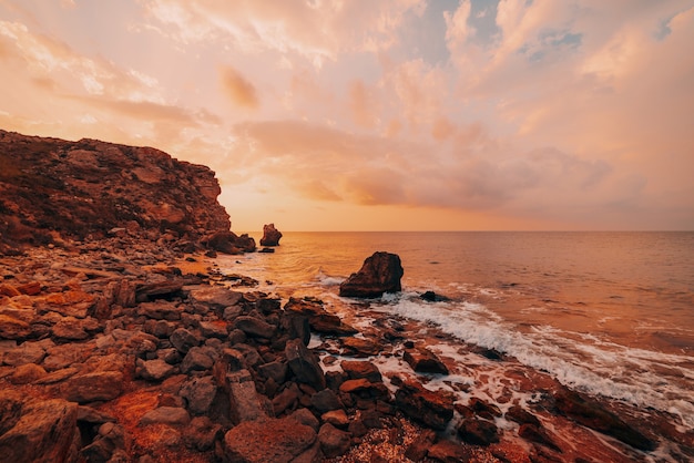 Amazing sunset at sea, beauty of nature. Scenic view of the sea, rocky coastline and sandy beach, golden sky and sun