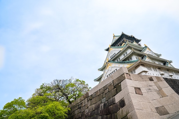 the amazing upward view of osaka castle with trees and blue sky in kansai of japan .