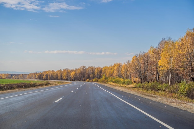 Amazing view with colorful autumn forest with asphalt mountain road. Beautiful landscape with empty road, trees and sunlight in in autumn. Travel background. Nature