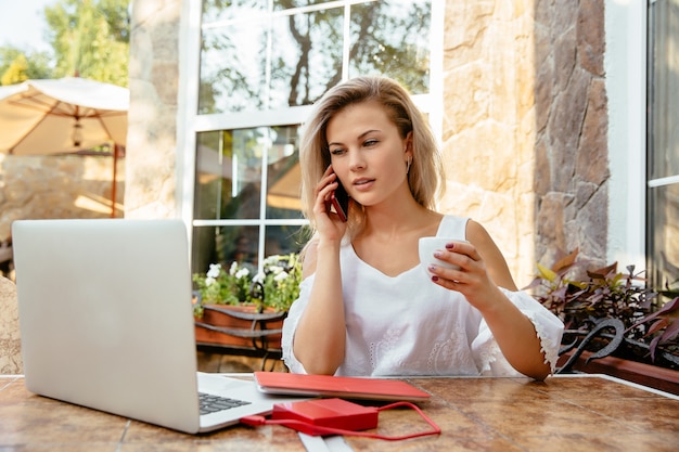 Amazing young woman talking by mobile phone and drinking a coffee at restaurant