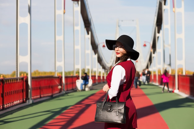Удивительная молодая женщина в модной одежде и аксессуарах, позирует на мосту. Место для текста