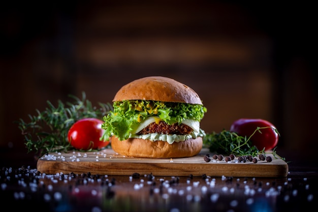 Ambachtelijke knapperige kipburger met kaas, sla, tomaat en saus op houten achtergrond