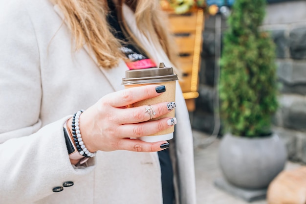 Ambachtelijke papieren koffiekop in handen van de vrouw met perfecte manicure Drinken van koffie om mee te nemen Nagelherfstconcept