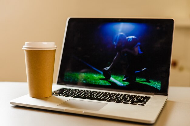 Ambachtelijke papieren koffiekopje in de buurt van laptop, nieuws