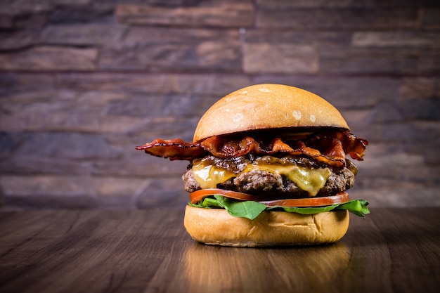 Ambachtelijke rundvleesburger met kaas, spek, gekarameliseerde ui en rucola op houten tafel