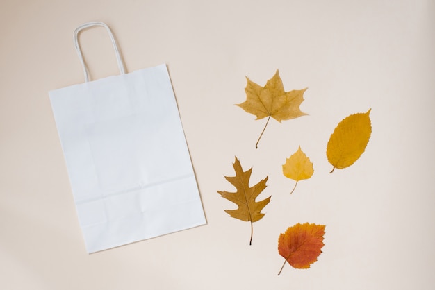 Ambachtelijke tas wit voor uw aankopen met herfstbladeren op een achtergrond van beige papier. Herfst concept. bovenaanzicht kopie ruimte