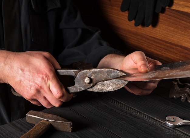 Ambachtsman snijdt dunne roestvrijstalen plaat met knipsels. Handen van de meester close-up. Werkomgeving in de werkplaats