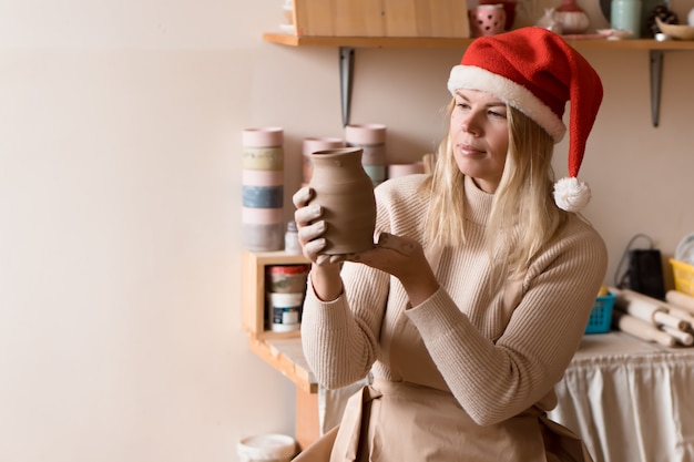 ambachtsvrouw in kerstmuts die geschenken maakt met de handen in een pottenbakkerij