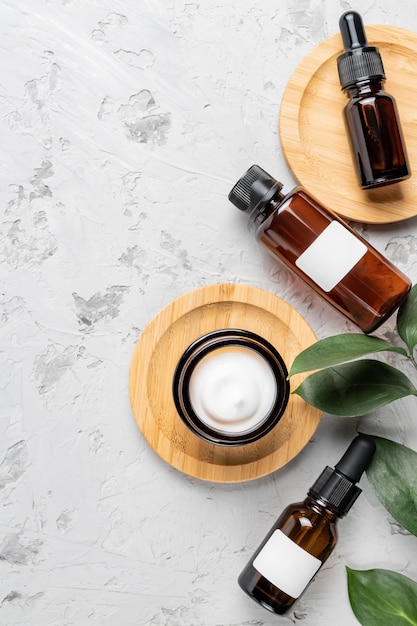 Amber glass bottle of organic cosmetics and green plant leaf on gray concrete background. SPA natural beauty products set. Flat lay, top view.