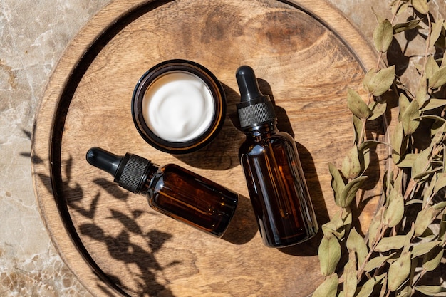 Amber glass bottles and jars with natural cosmetics and eucalyptus on wooden tray on table in bathroom SPA organic bio cosmetics set