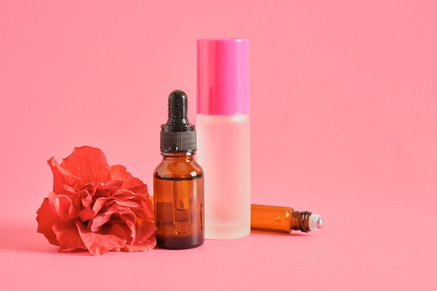 Amber glass dropper bottle and perfume bottle and hibiscus flower on pink background copy space mock up